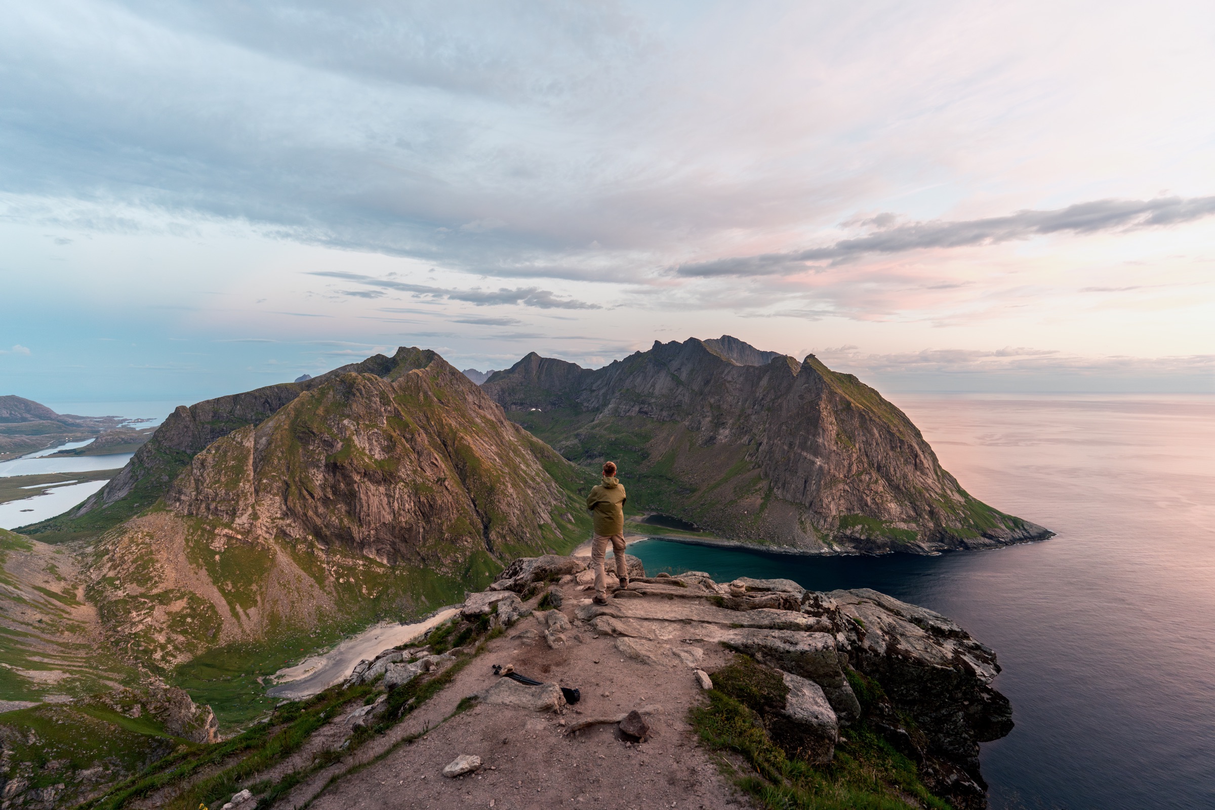 Hiker overlooking mountain peaks and a fjord at sunset