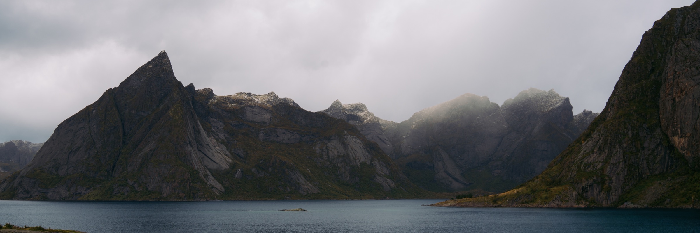 Clouds gathering around sharp mountains beside a fjord